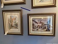 Two framed art pieces hanging on a wall showing street views, one labeled Antwerp Belgium, the other Portugal