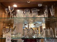 Wide view of shelves showing various glassware and salt and pepper shakers arranged on glass shelves inside wooden cabinet.