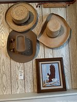 Three hats hanging on a wood panel wall along with a framed eagle picture below them