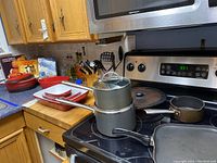 Kitchen countertop and stove with visible Lagostina cookware including clay Dutch ovens, pots, pans, utensils, and cookbooks