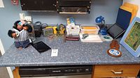 Wide view of the countertop displaying assorted office items including a small doll, calculators, organizers, lamp, framed art, and tablets