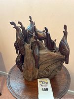 Front view showing nine dark polished wood birds perched on a natural wood tree stump base, placed on a small round wooden table.