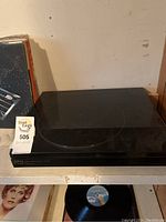 Closed view of black Akai turntable with dust cover on, showing overall condition and shelf placement next to vinyl records.