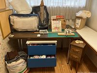 Wide shot showing the crafting table, batting, books, yarn in drawers, fabric in bag, and small wooden side table with three drawers.