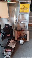 Photo showing the shop vac, ladder, manuals, box of hand tools, shovel, and saw in garage setting
