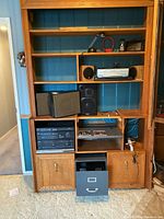 Wide view of wooden shelving unit with stereo system components, speakers, lamp, phone, and filing drawer inside.