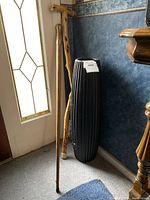 Tall black vertically ribbed vase with label on top, placed on floor near door