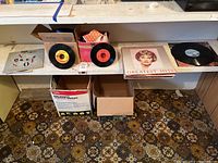 Wide angled photo showing multiple vinyl records laid on shelves including 45 RPM singles and full albums.