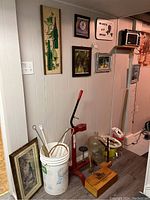 Wide view showing wine making tools including bottle capper, bucket with tools, glass carboy, framed art on walls, and shelf with GE AM/FM radio.