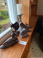 Four wood carvings and a candle holder displayed on a wooden windowsill with garden view.