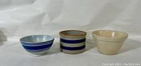 Front view of three antique English bowls including a blue banded earthenware bowl, a cylindrical RRP Co. banded crock, and an ivory stoneware bowl.