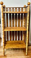 Front view of 3 tier bamboo and pine shelf etagere showing bamboo posts with rounded finials and pine shelves