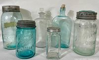 Photo of six antique glass bottles and fruit jars including blue Ball Perfect Mason jars and clear glass bottles with various metal and cork lids