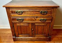 Front view of antique walnut cabinet showing two drawers with original brass hardware and two paneled doors below with a single knob.