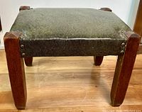 Front view of the early 1900s oak stool showing upholstered seat with brass rivets and oak legs.