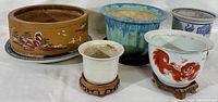 Five assorted Chinese planters, showing pottery, porcelain, hand-painted and glazed designs, along with accompanying underplates and wood stands.