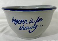 Side view of white pottery bowl with blue rim and text 'Popcorn is for sharing...' in cursive blue paint on the outside.