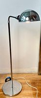 Full view of chrome floor lamp, lamp lit, showing round base and straight pole