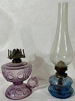 Pair of old glass oil lamps: pressed glass amethyst finger lamp and blue blown glass lamp with chimney shown side by side