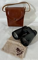 Binoculars, beige branded cleaning cloth, and brown leather case arranged together.