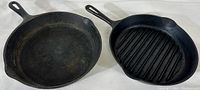 Two cast iron skillets placed side by side, one smooth surface and one ribbed grill surface, both with handles and twin spouts.