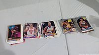 Photo showing four stacks of basketball cards laid out on a table. Cards show different NBA players from the 1990s era, with varying card back designs and front images.