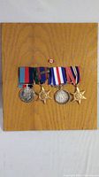 Four World War II era medals mounted on an oak plaque, displaying their ribbons and a small Canadian flag pin above.