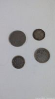 Overview photo of four old coins with extreme wear on white background showing size and condition.