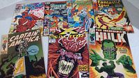 Seven Marvel comic books shown spread out on a surface, covers visible with superheroes like Spider-Man, Captain America, and Hulk.