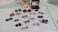 Full overview of all 19 pairs of cufflinks arranged on table, showing variety of styles including boxed and unboxed items