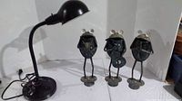Photo of three metal frog figurines and a black metal adjustable desk lamp showing full lot
