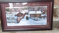 Full view of framed winter farm scene print showing farmhouse, barns, horse, sleigh, and snowy landscape within wooden frame and maroon mat.