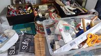 Overall view of multiple bins and tins filled with sewing supplies including patterns, scissors, thread, and small containers.