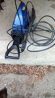 Front and side angle of the blue Simoniz pressure washer showing power cord, spray gun with trigger and high-pressure hose.