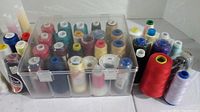 Plastic container with multiple colors of thread spindles arranged inside and outside, showing diversity in thread colors and spool sizes.