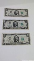 Front view of three 1976 series US two dollar bills, showing Thomas Jefferson portrait and serial numbers.