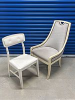 Photo showing two white chairs: a white wooden chair with upholstered seating and an upholstered armchair with decorative trim