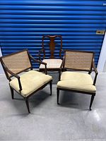 Three wooden armchairs shown together, two have cane backs and the third has a solid decorative wooden back. Cushioned seats are beige. The chairs show signs of dust and use, requiring cleaning.