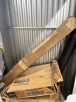 Photo showing large rectangular cardboard box leaning vertically in storage, appears to be packaging for the projector screen.