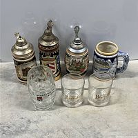 Full view showing all seven beer mugs and steins on concrete surface.