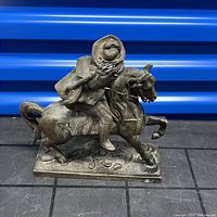 Side view of bronze cowboy statue riding a horse with detailed cowboy attire and horse movement.