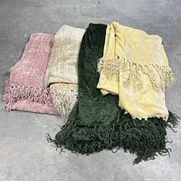 Four chenille blankets folded and stacked showing colors and fringe detail on concrete floor