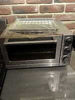 Front view of the stainless steel Cuisinart toaster oven with oven rack and tray on top, wrapped in plastic.