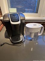 Front view of Keurig coffee maker and Brita pitcher on countertop near window.