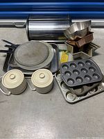 Overview of kitchen and baking items arranged on the floor including storage jars, various baking pans, and bread box.