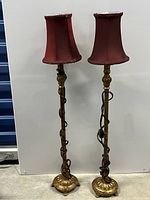 Full view of both floor lamps showing their ornate twisted stems, gold-tone bases, and red fabric shades.