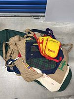 Overview of mixed fabric bags and three yellow Kahlua aprons laid on green surface