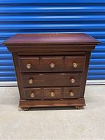 Front view of small wooden dresser showing six drawers and brass knobs.
