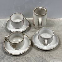 Four stoneware cups with matching saucers and one creamer pitcher, displaying the floral pattern and overall condition.