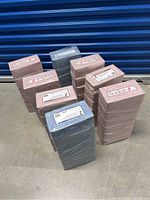 Multiple packs of Skilcraft Facial Tissues stacked on floor, some pink, some grey wrapped in plastic.